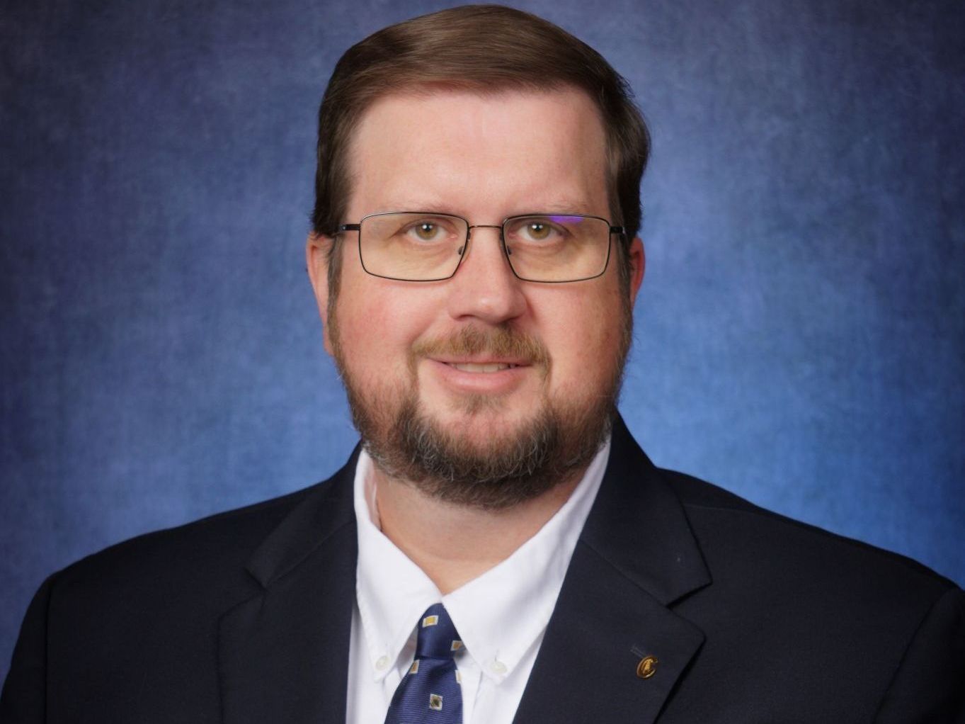 A man with a beard and glasses is wearing a suit and tie.