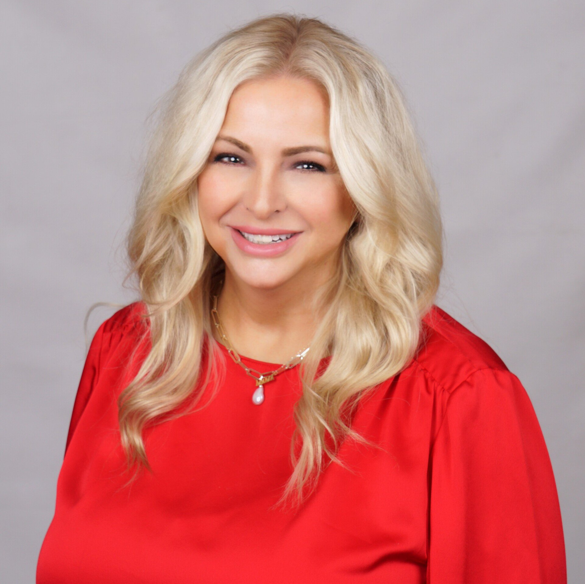 A woman with blonde hair is wearing a red shirt and a necklace.
