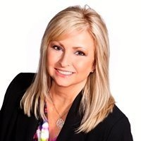 A woman wearing a black jacket and a necklace is smiling for the camera.