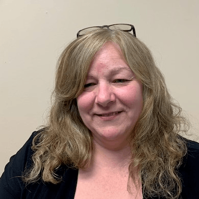 A woman wearing glasses and a black jacket is smiling for the camera.