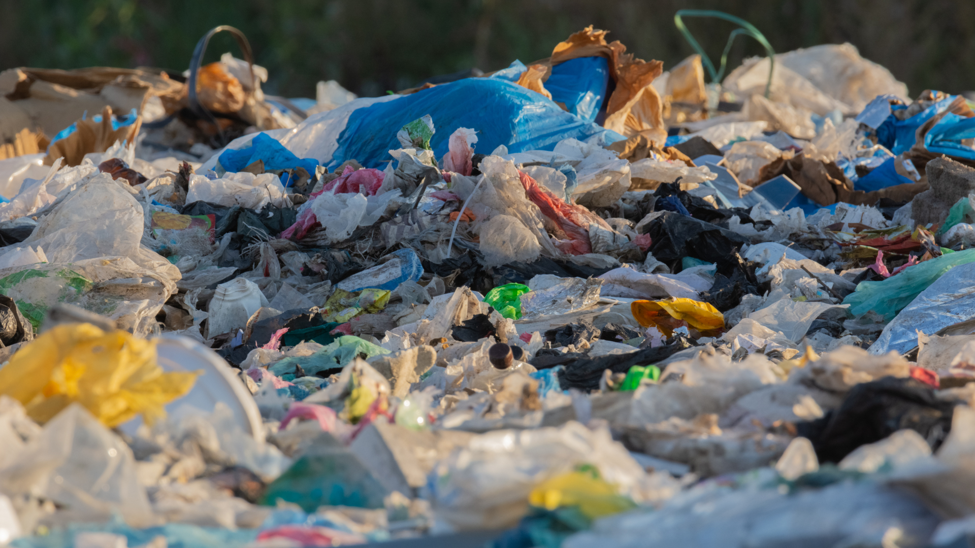 Pile of colorful plastic waste at a landfill site, in sunlight.