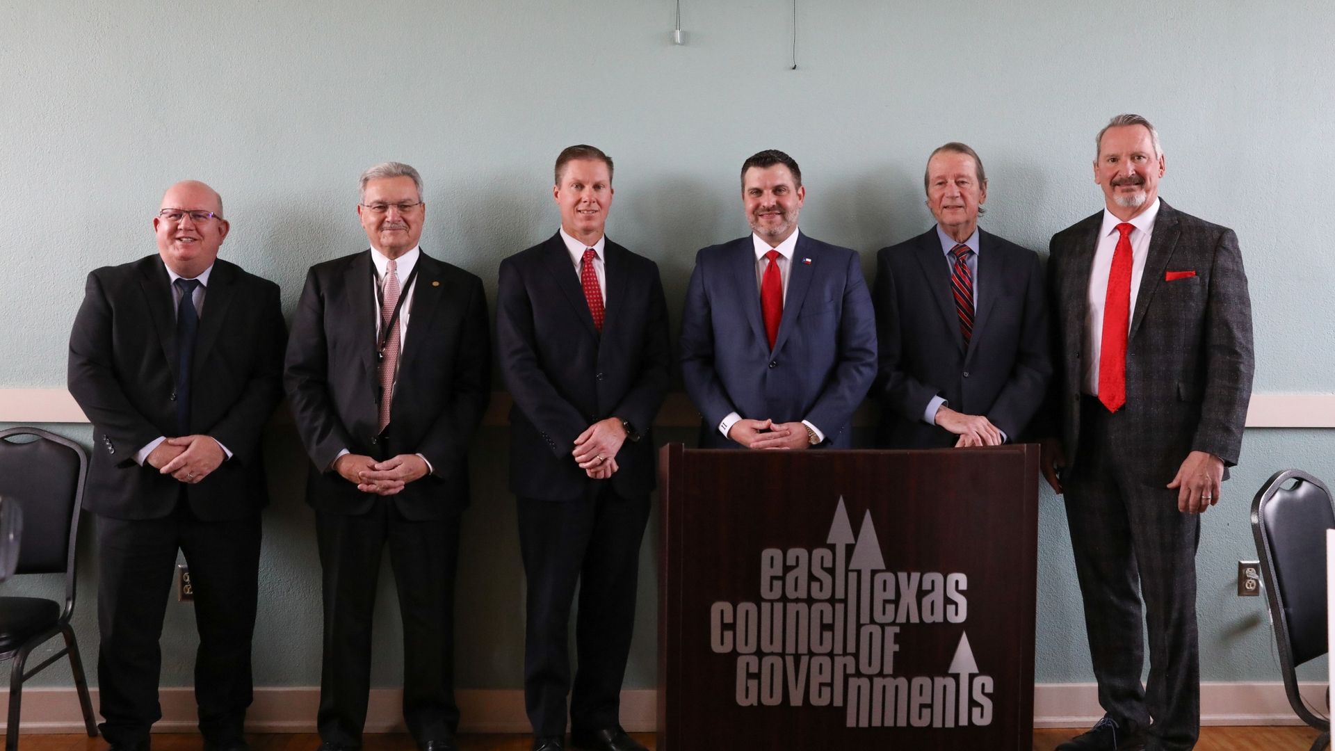 a group of men standing in front of a east texas council of governments podium