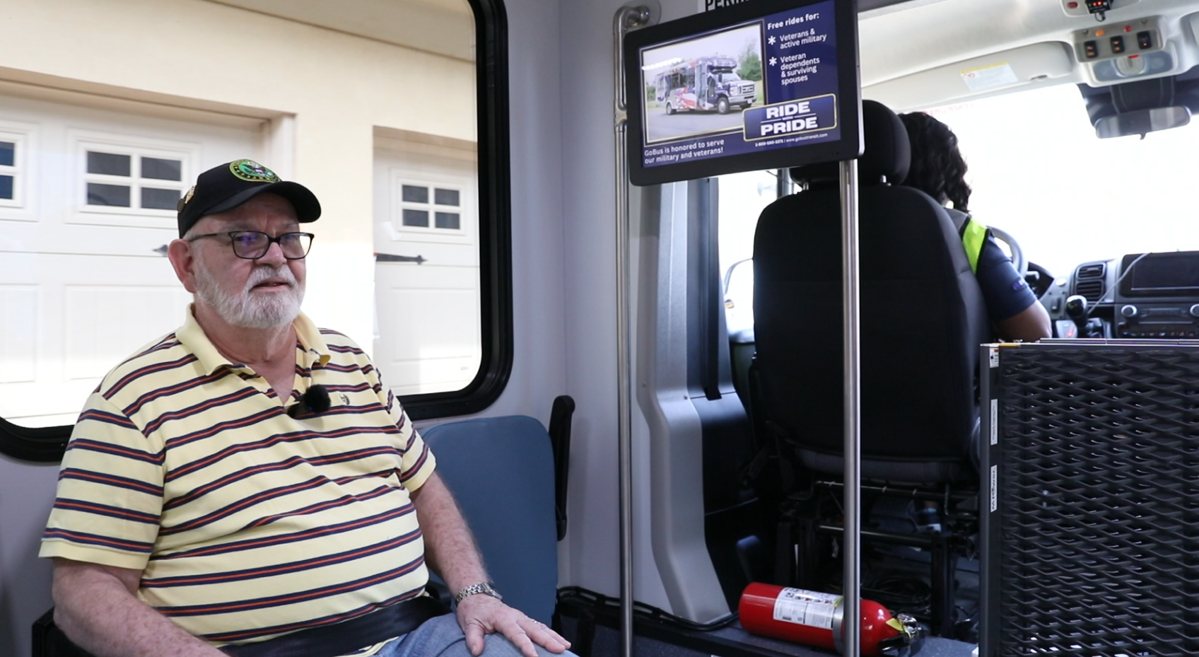 A man in a striped shirt is sitting in a car with a tv on the wall.
