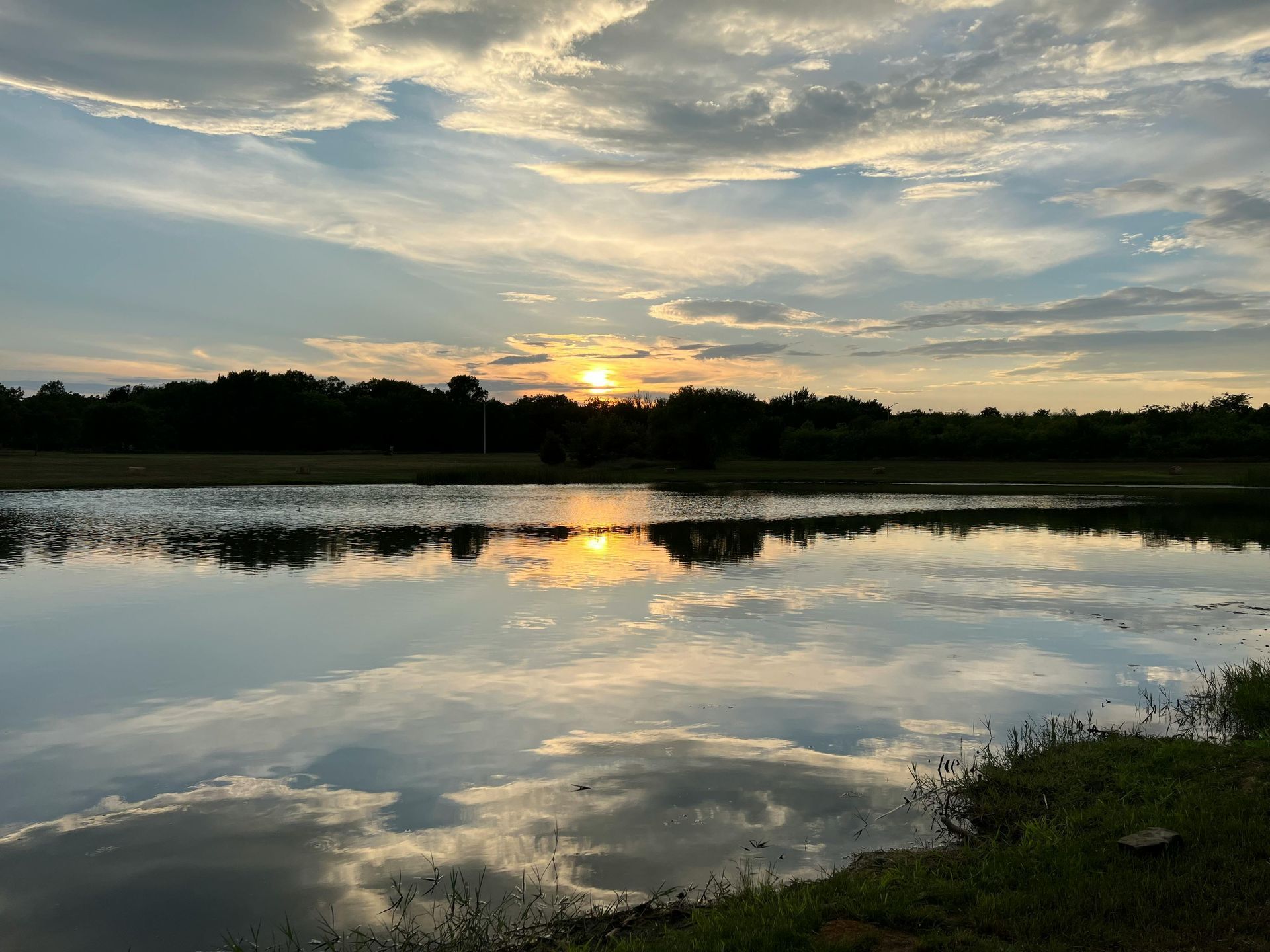 Sunset over a calm lake with clouds reflected in the water and a tree-lined shore