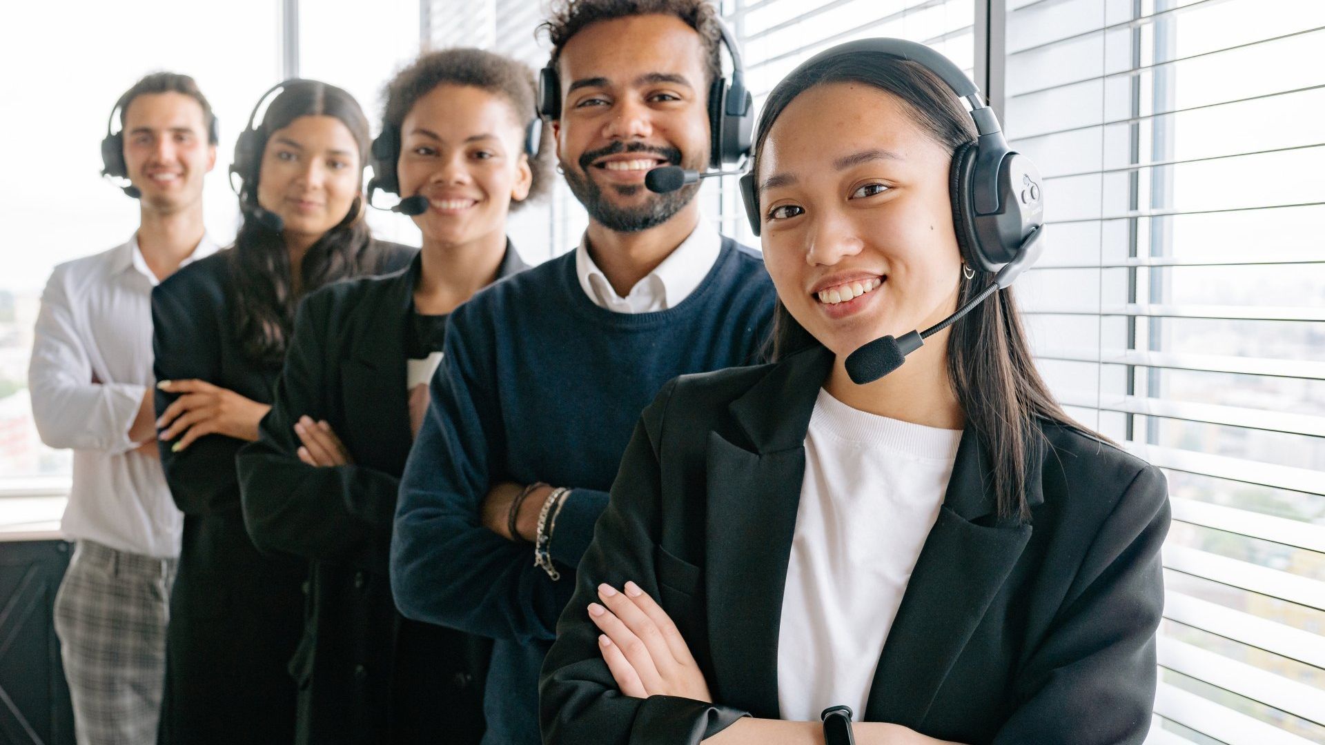 A group of people wearing headsets are standing next to each other in front of a window.