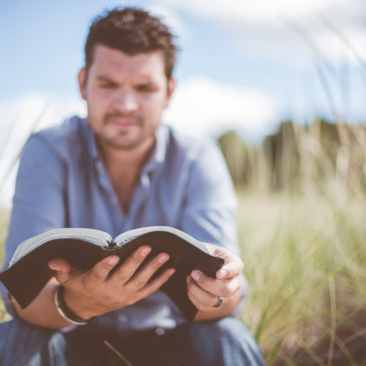 A man is sitting in the grass reading a bible