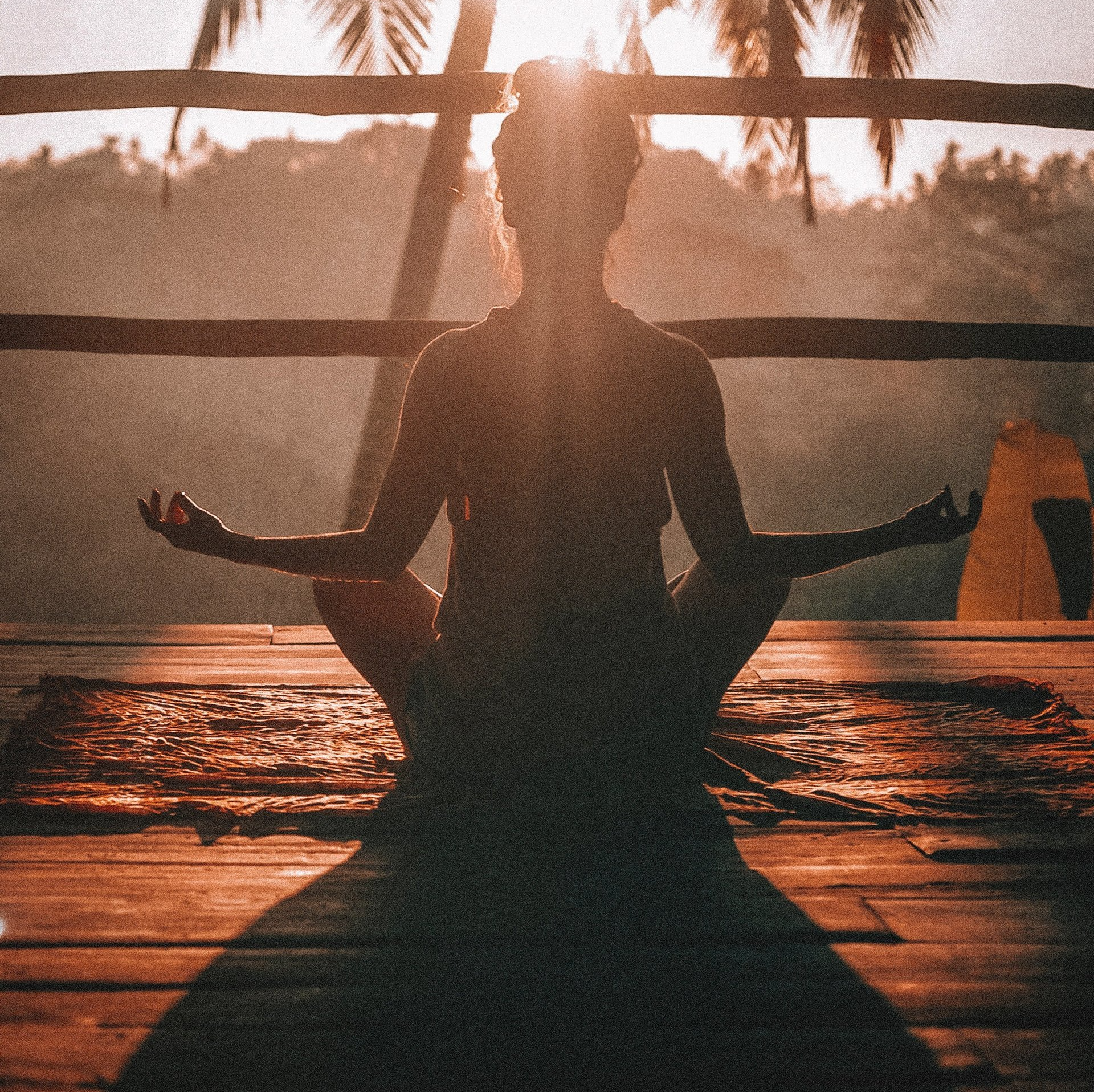 A woman sits in a lotus position on a wooden deck at sunset