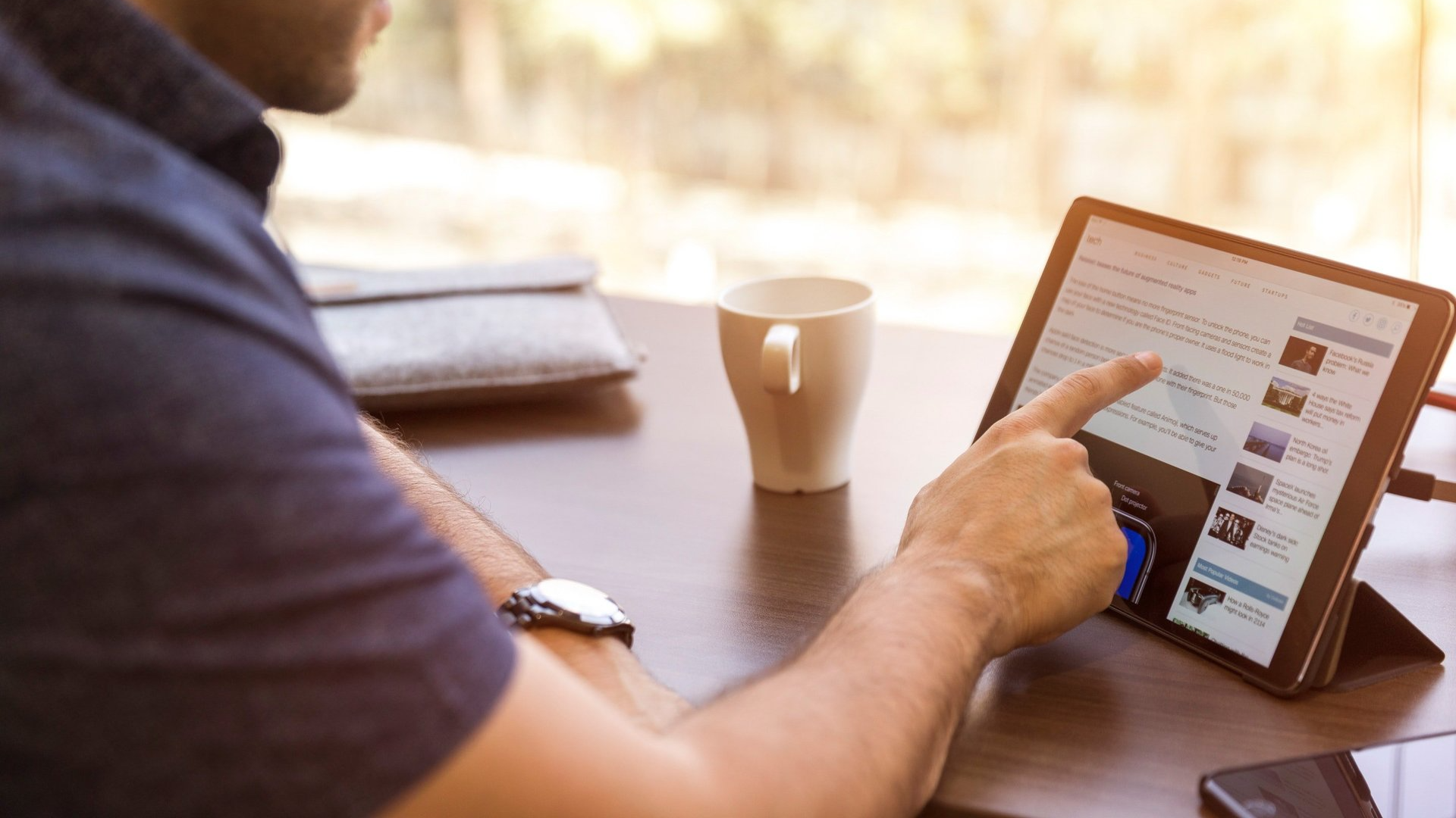 A man is sitting at a table using a tablet computer.