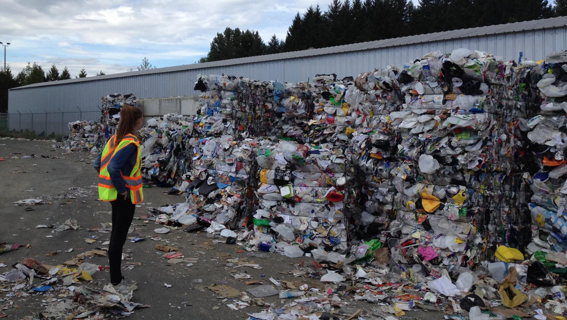 A woman is standing in front of a large pile of trash.