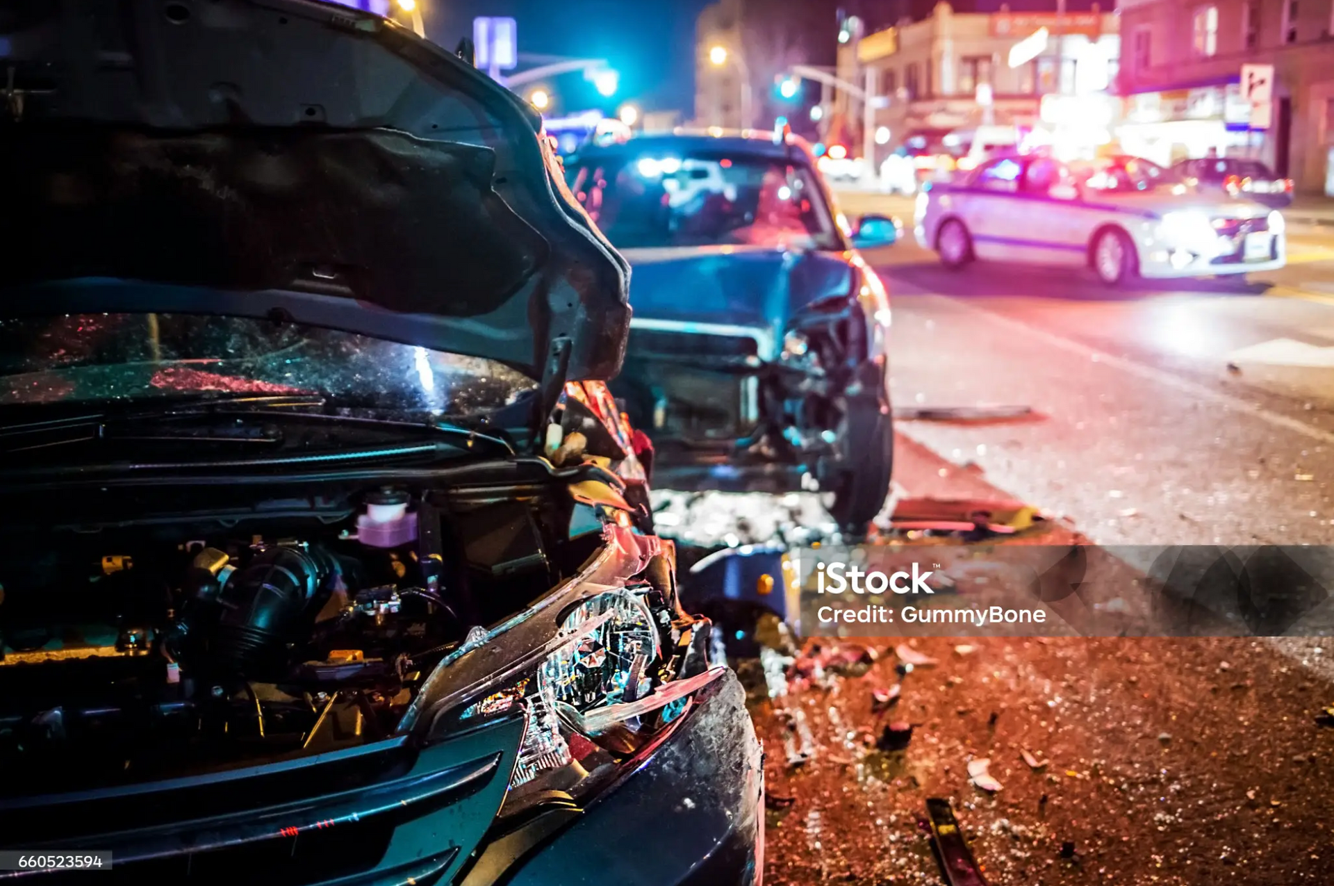 Close-up of two damaged cars at night with police lights in the background.