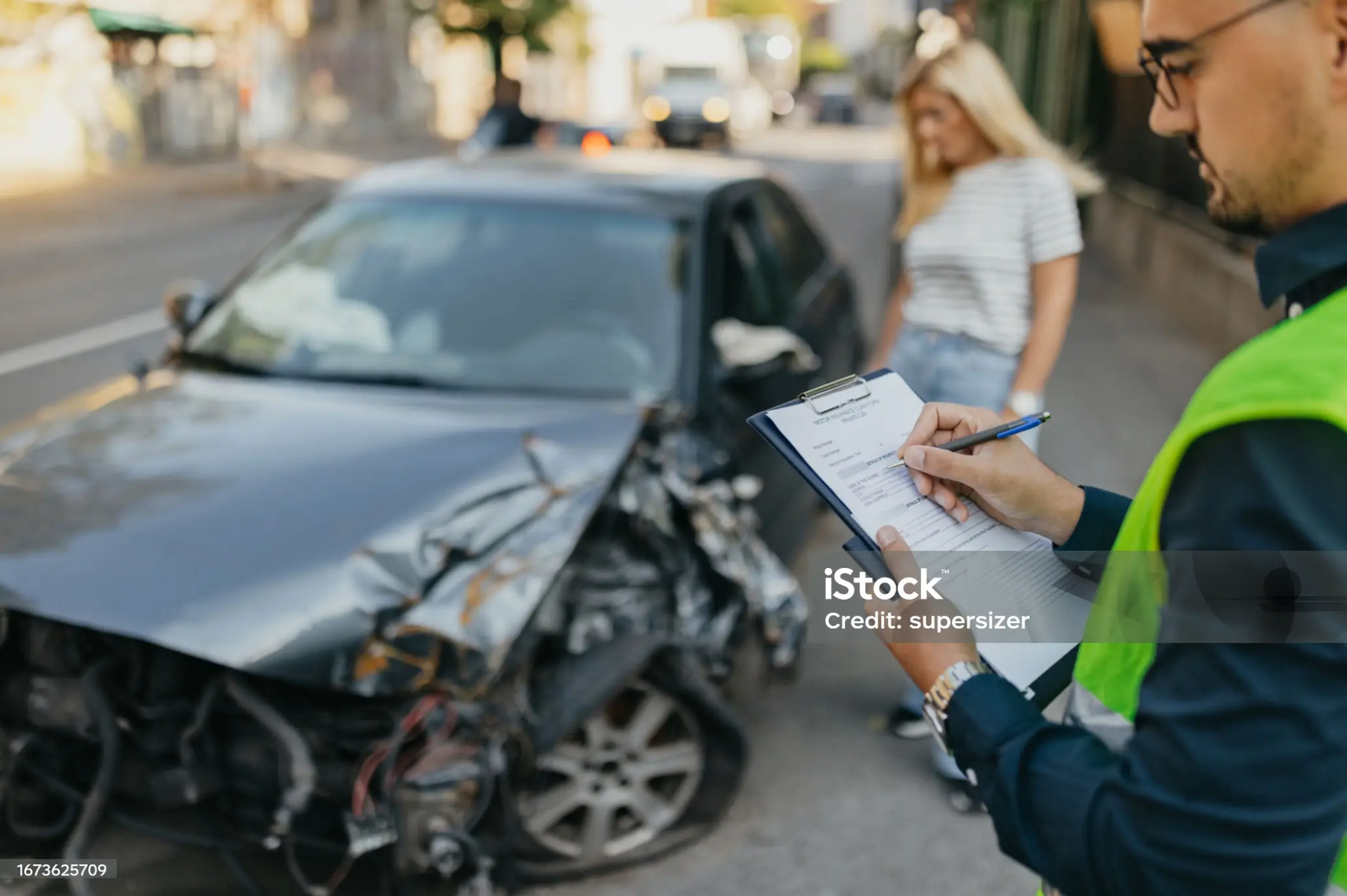 Insurance adjuster documenting a car accident while a concerned driver looks on.