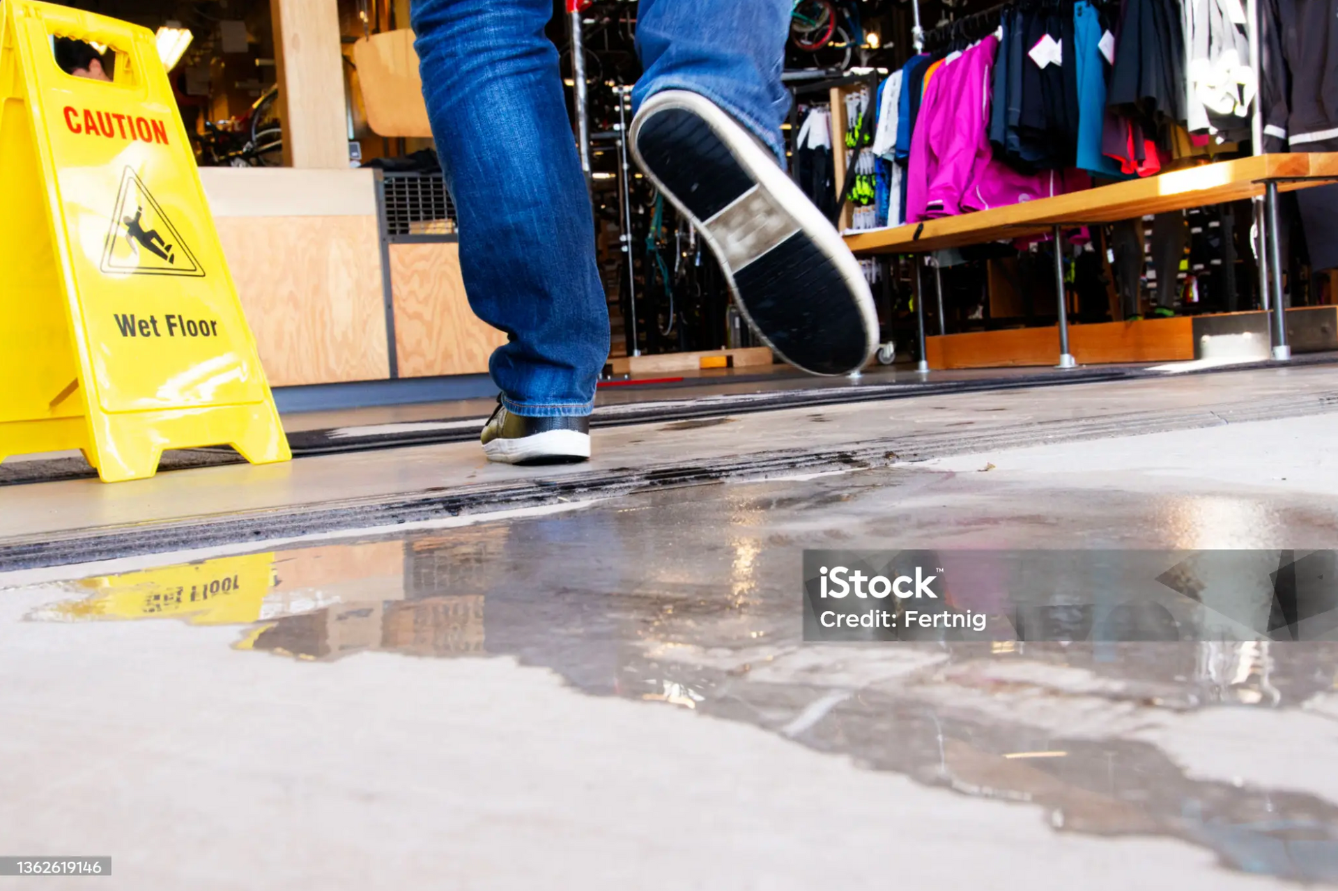 Person walking by a wet floor sign in a retail store, warning of potential slip and fall hazards.