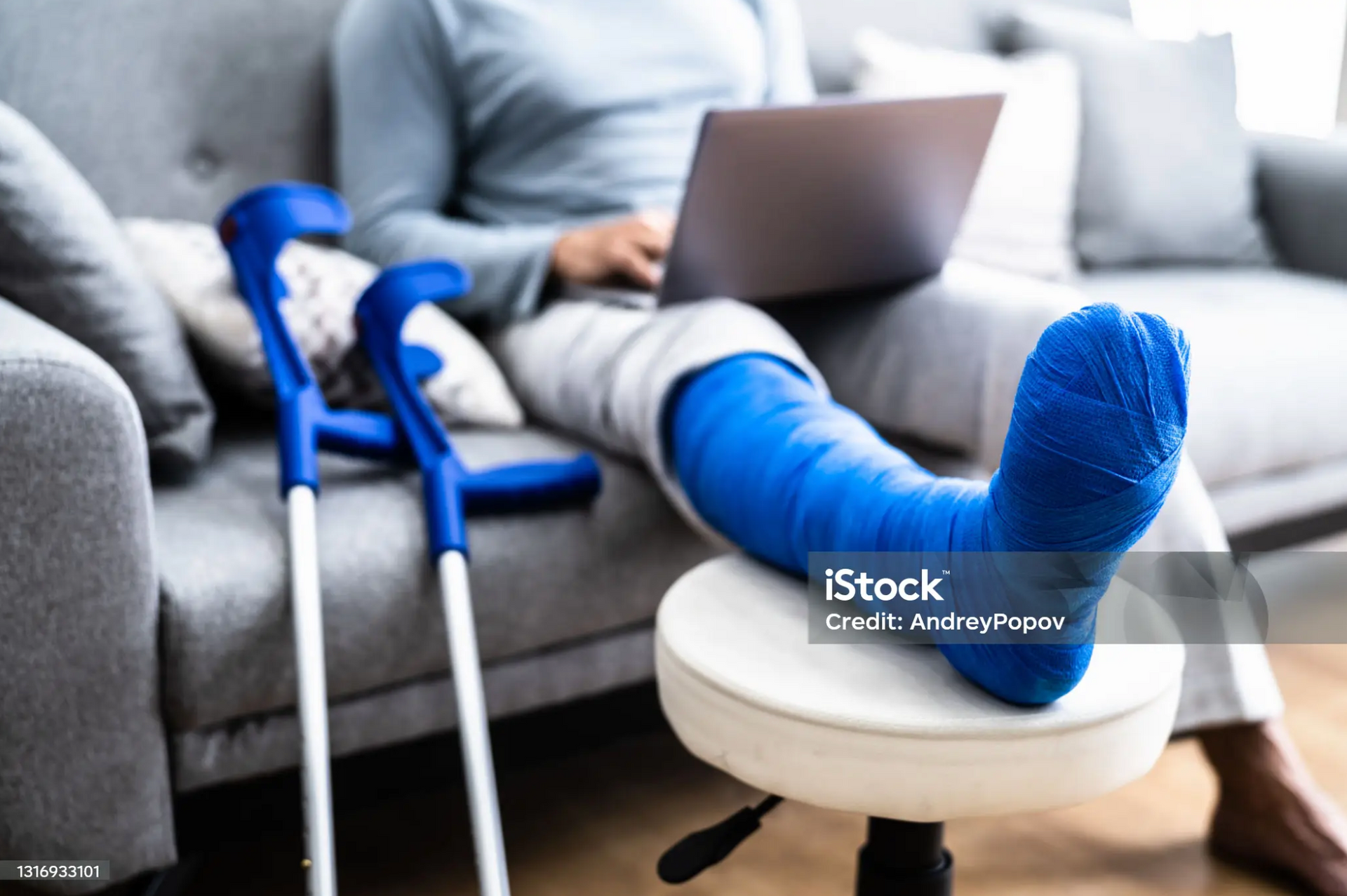 Person with a leg cast sitting on a couch with crutches beside them, filling out a disability claim form.