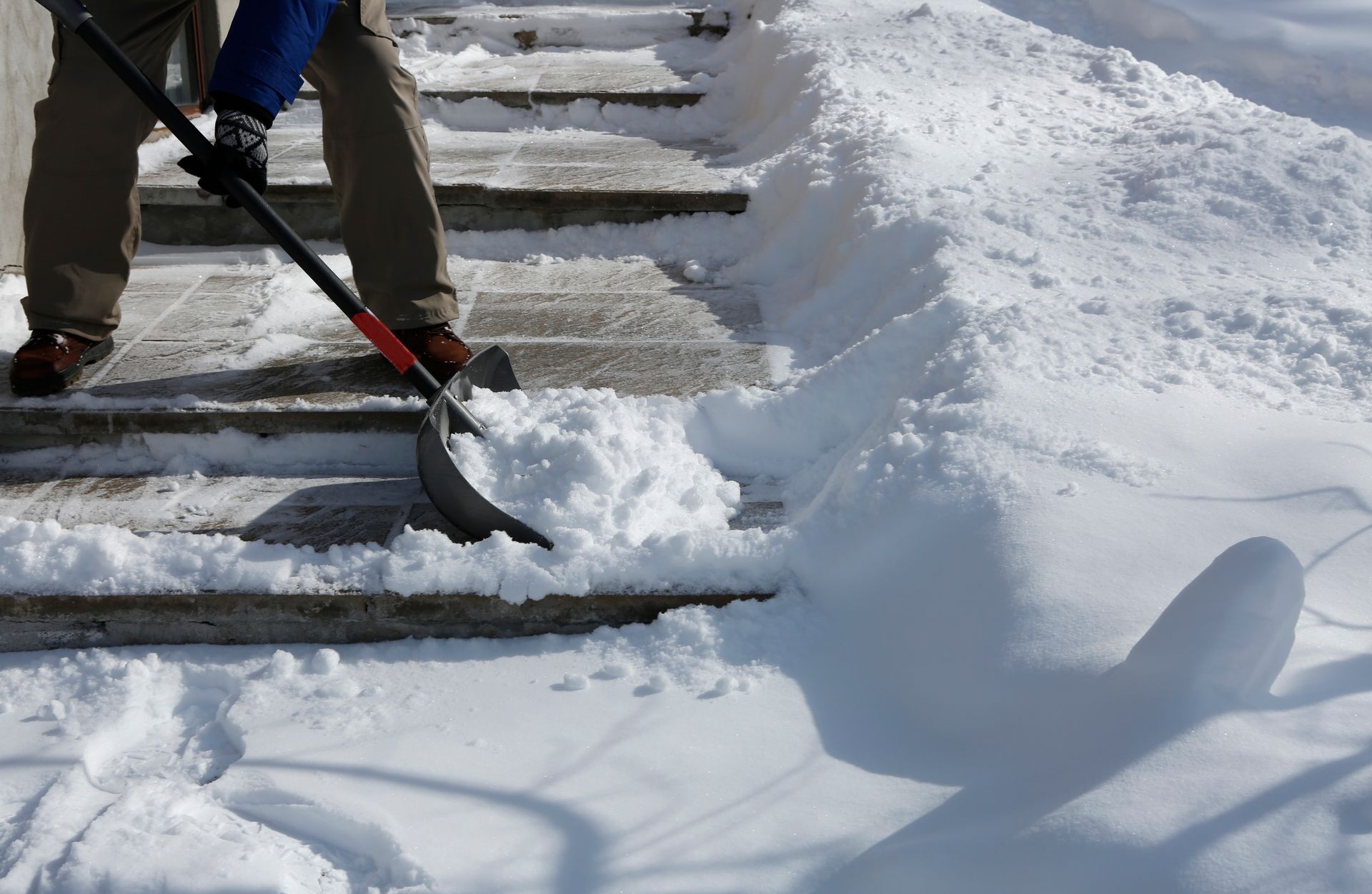Person shoveling snow off outdoor steps to prevent slip and fall accidents.