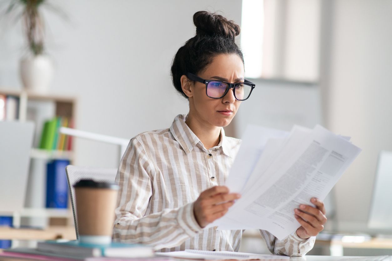 A concerned employee, sitting at her desk, reviews documents that pertain to a workplace investigation, symbolizing the need for the support of an employment lawyer during a workplace inquiry.