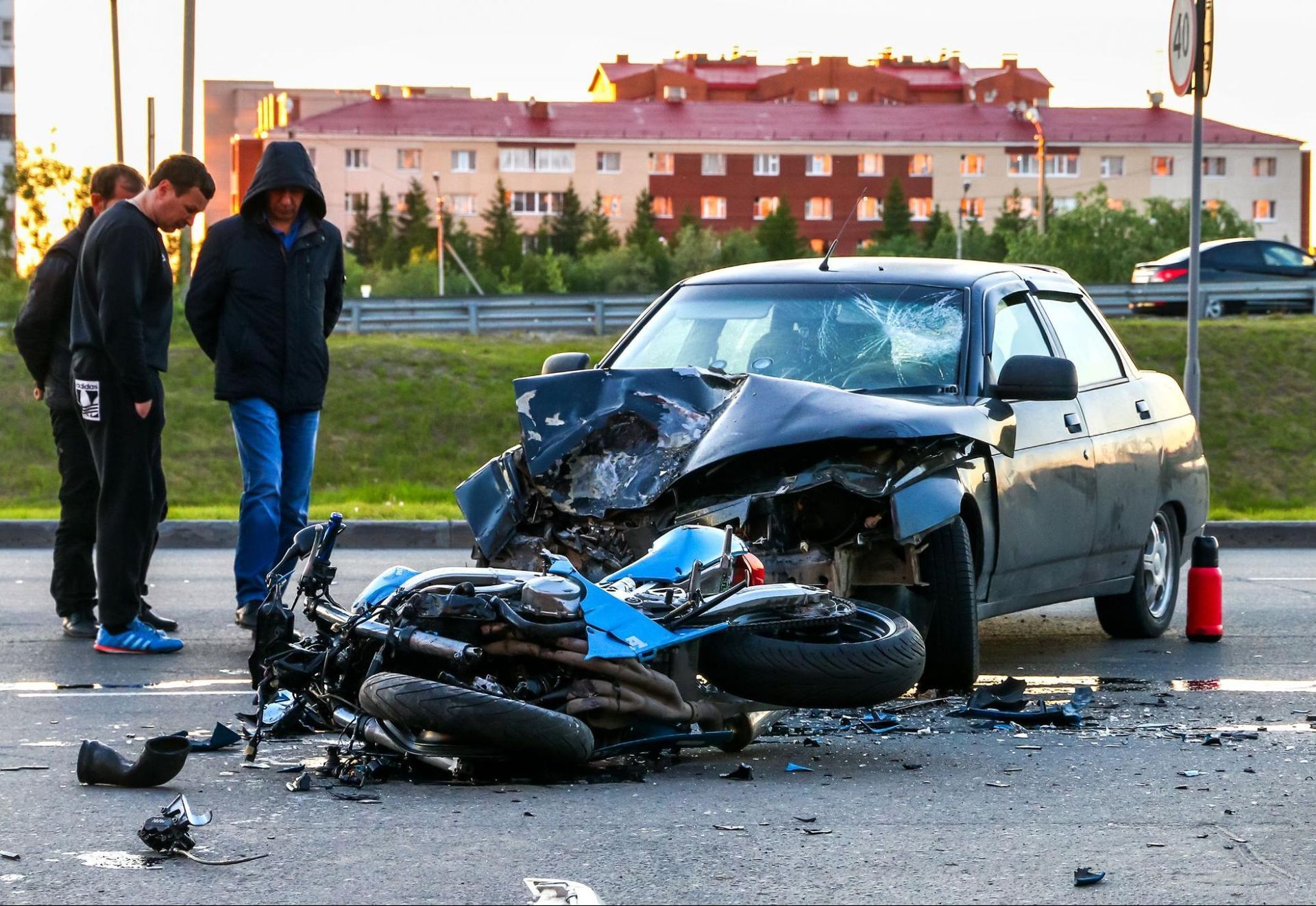 Three people standing next to a damaged motorcycle and car that have been in an accident.