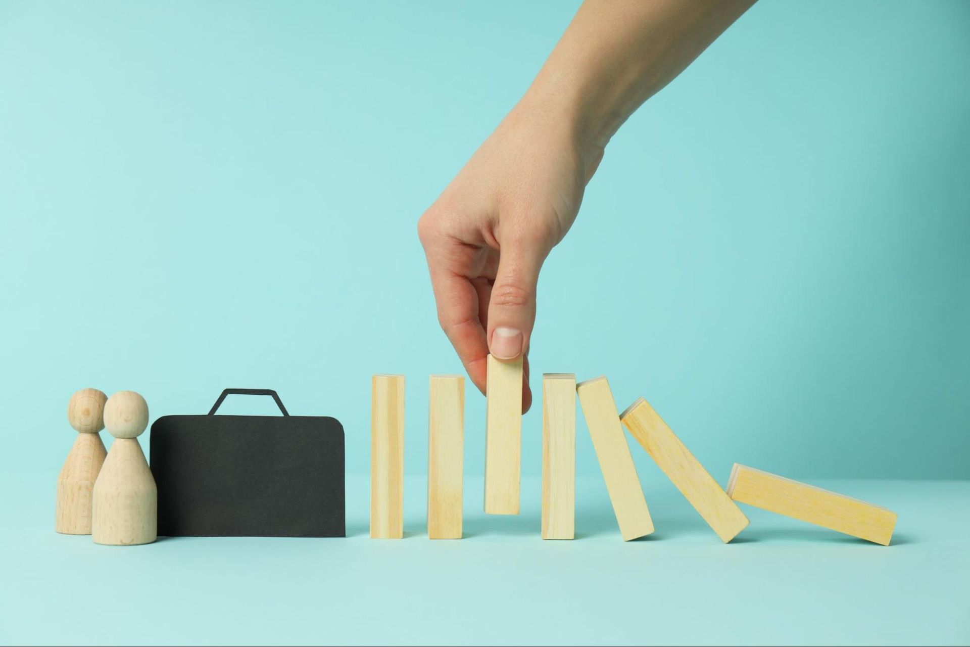 Blocks tumbling to one side towards a briefcase, with a hand holding barrier block in place.