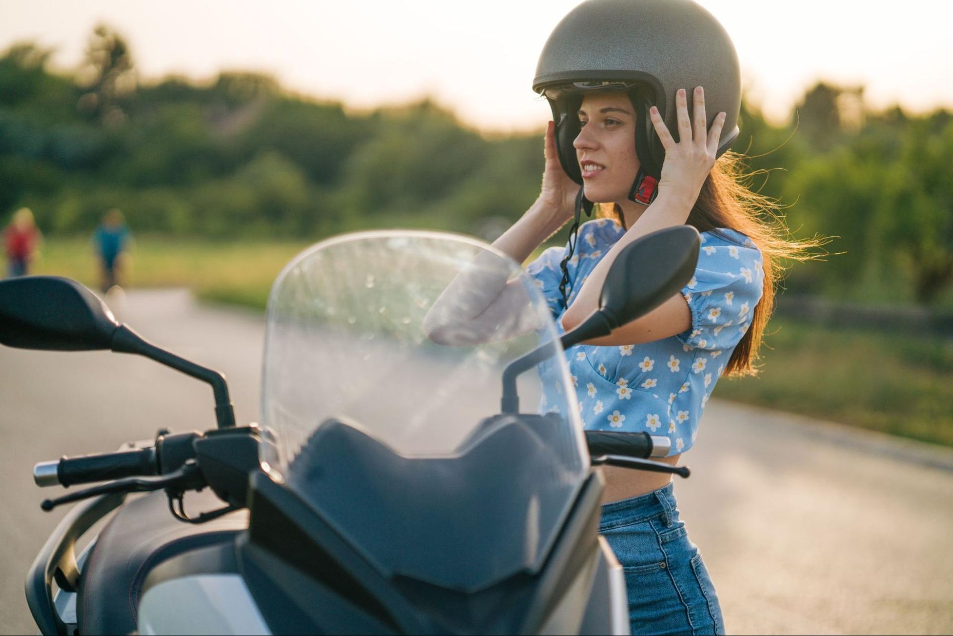 Woman about to get onto a motorcycle putting on a helmet.