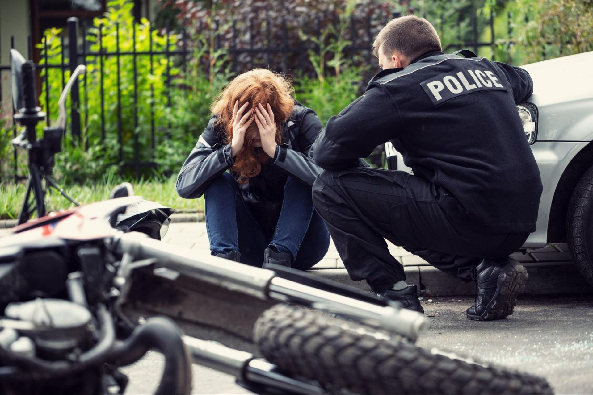 A motorcycle driver sitting on a curb holding their head next to a police officer after getting into a motorcycle accident.