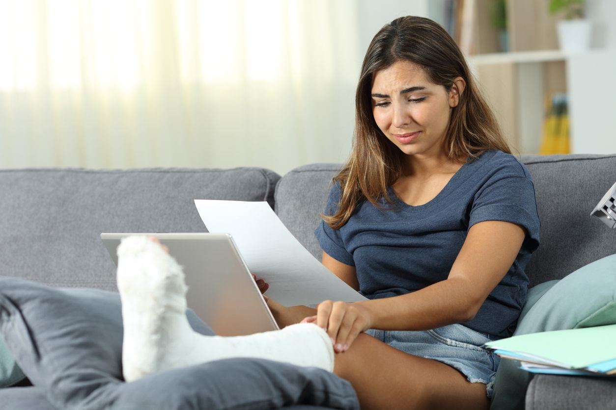 A worried woman with a leg cast reviews insurance paperwork at home, illustrating the need for a car accident lawyer to help navigate when a claim is denied.