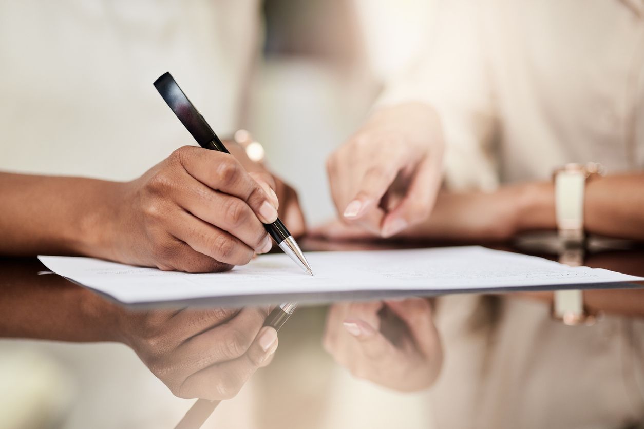 The hands of a life insurance lawyer and a client are pictured above a document as the review and signing of a life insurance document are taking place.