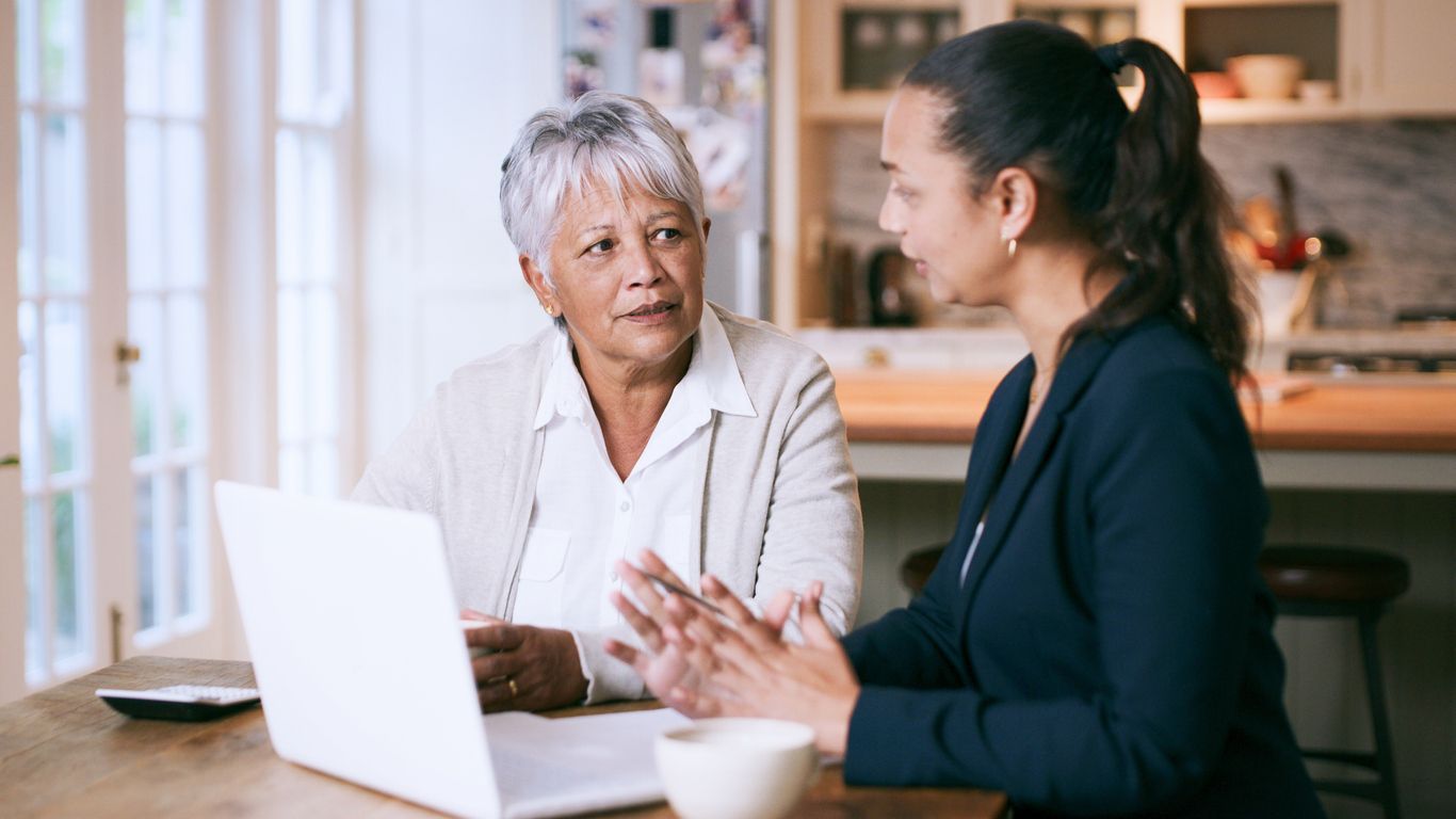 A life insurance lawyer consulting with an elderly client in a reassuring manner, seated at a table with a laptop.