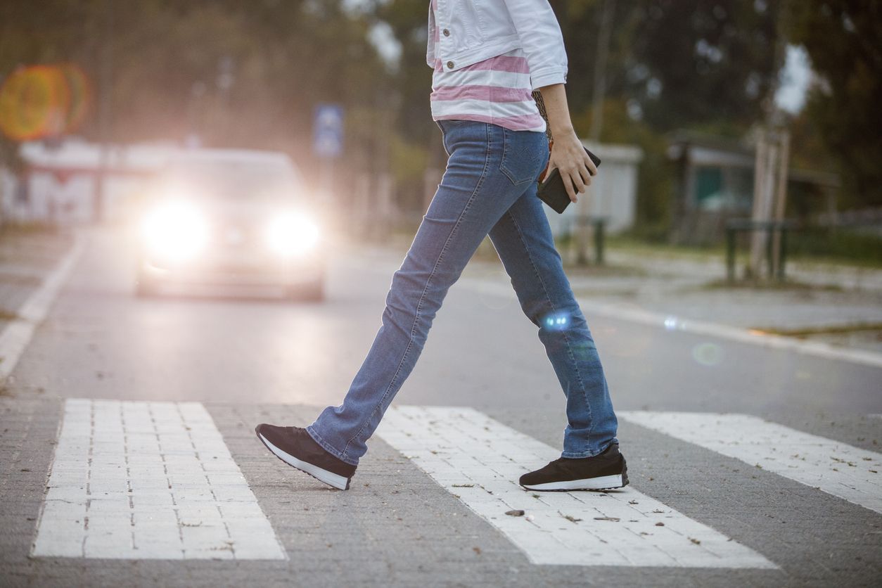 A person crosses a street at a crosswalk with car headlights approaching.