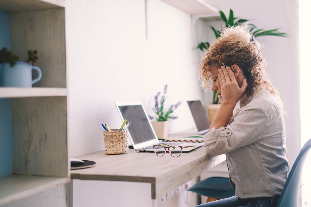 A person sitting at a desk, holding their head in frustration while reviewing a denial letter, with a laptop and glasses on the desk.