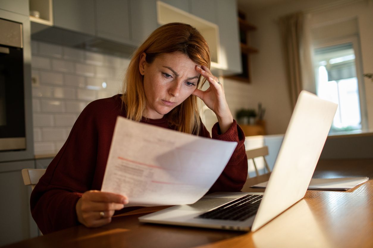 A concerned woman reviewing a denied life insurance claim letter while sitting at her kitchen table.