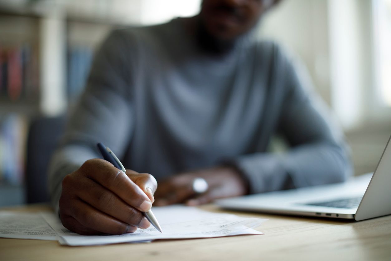 Close-up of a person reviewing severance package documents with a pen and laptop on the desk.