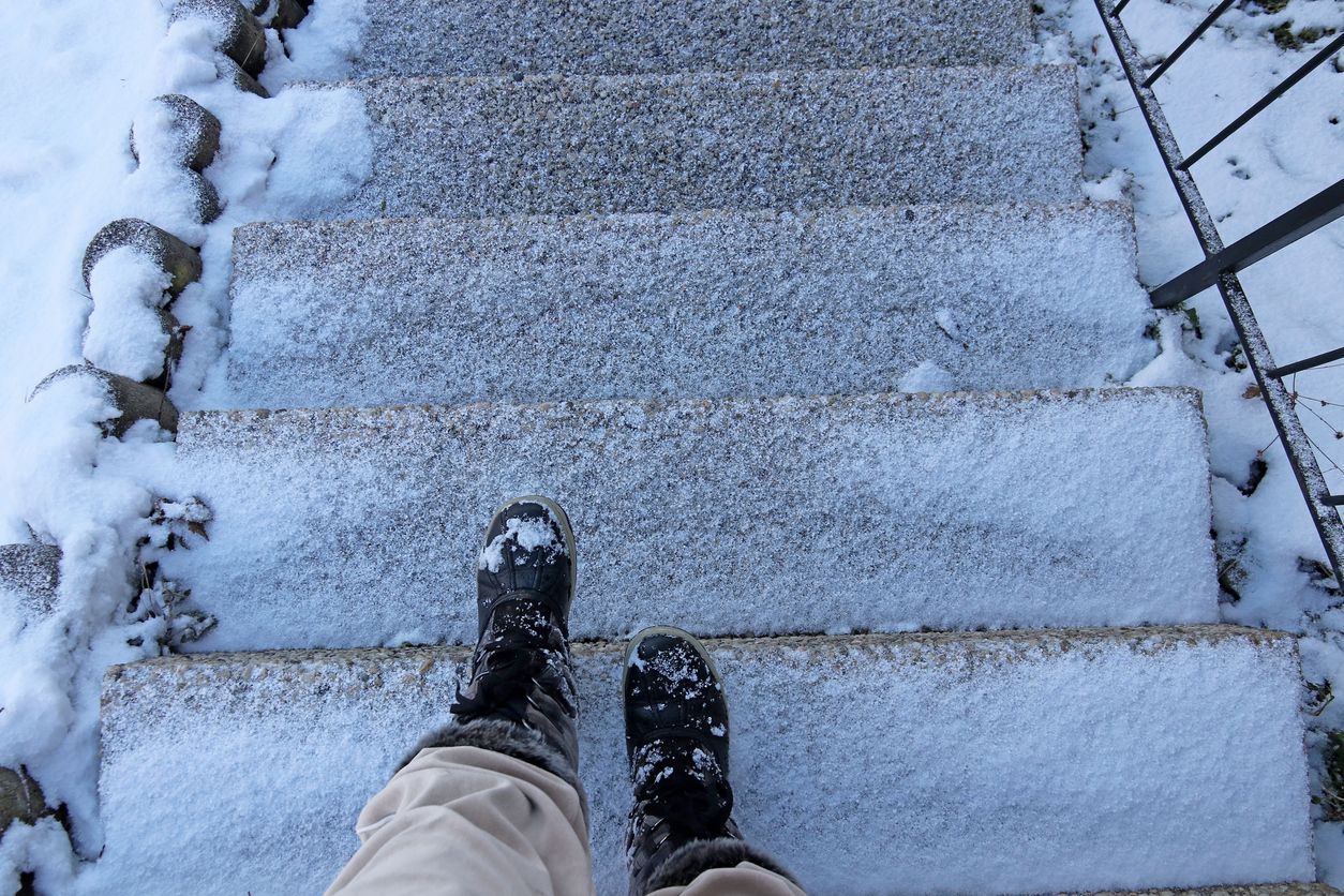 Close-up of a person's boots stepping on icy stairs, illustrating a common winter hazard that can cause slip and fall accidents.