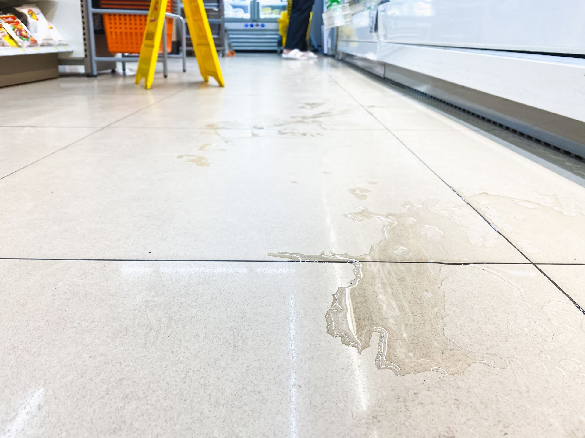 A wet floor in a store with a visible caution sign, highlighting the importance of hazard warnings to prevent slip and fall accidents.