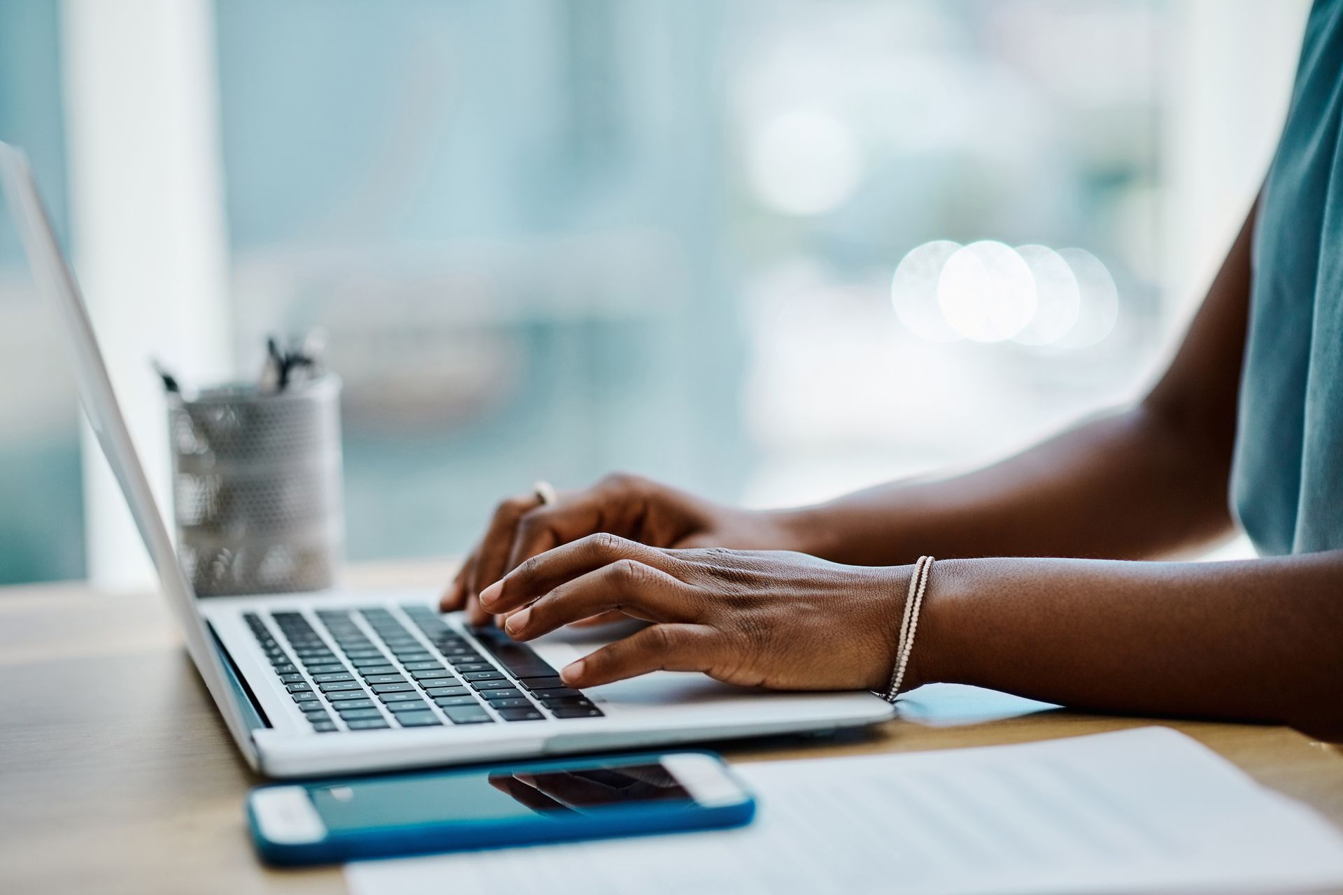 Close-up of hands typing on a laptop, with documents and a smartphone placed on the desk.