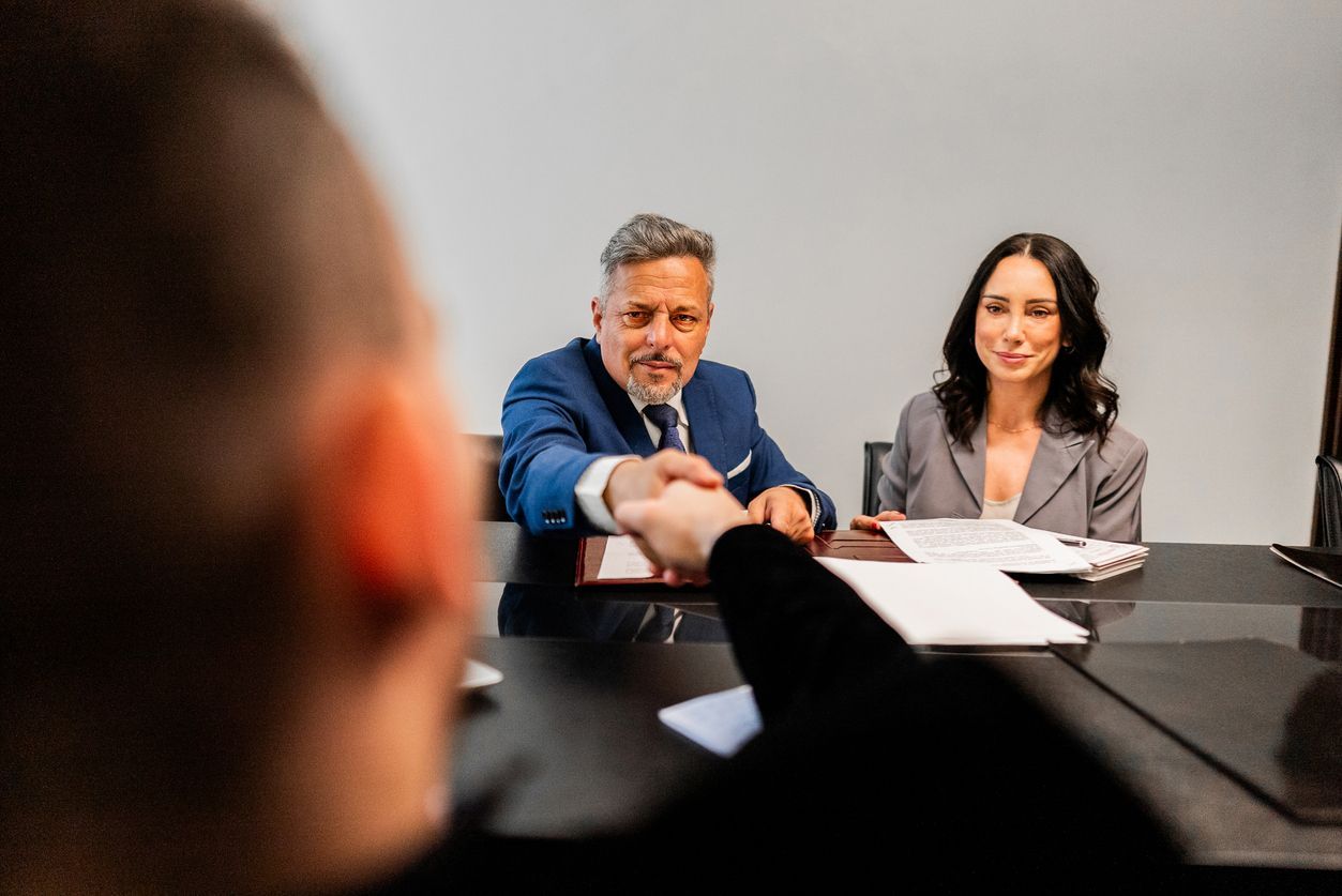 A professional legal team shakes hands with a client across the table, representing wrongful dismissal lawyers providing support during a workplace investigation.