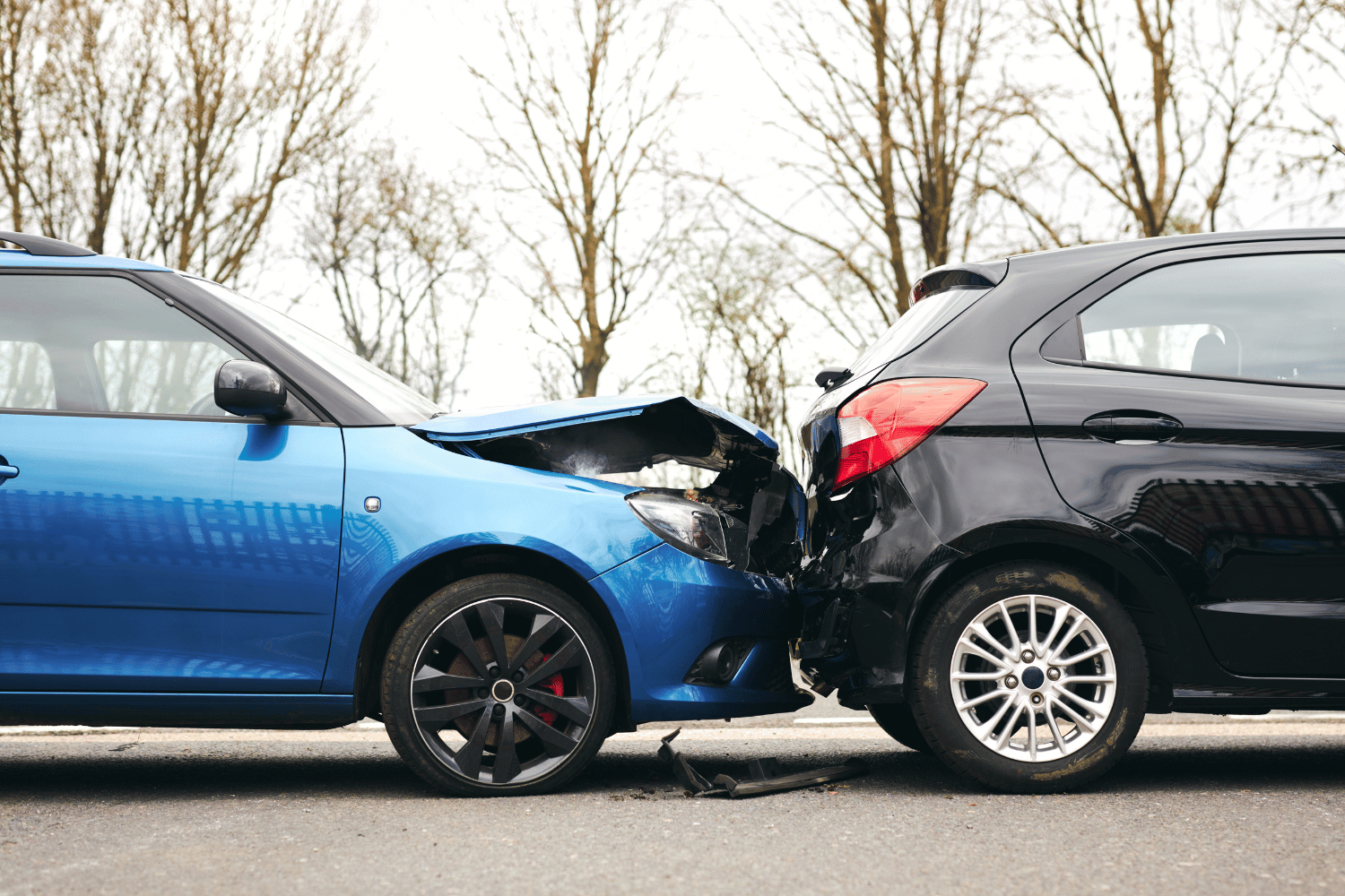 Two cars, blue and black, with front ends crushed in a rear-end collision on a road