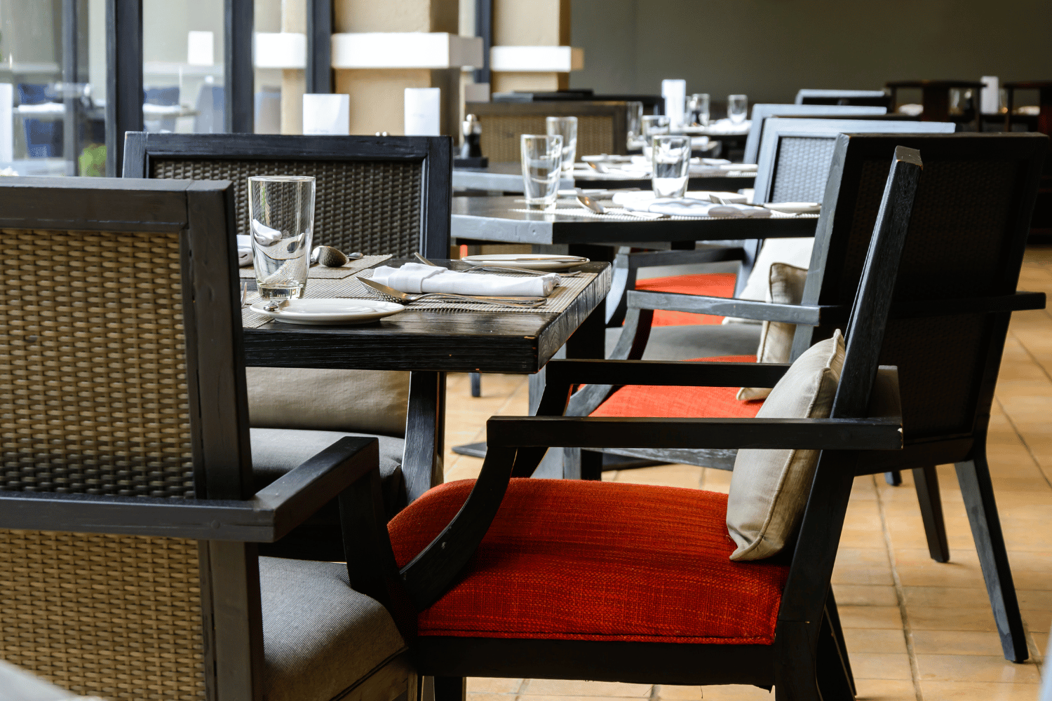 Empty restaurant tables with black chairs and red cushions in a bright dining area