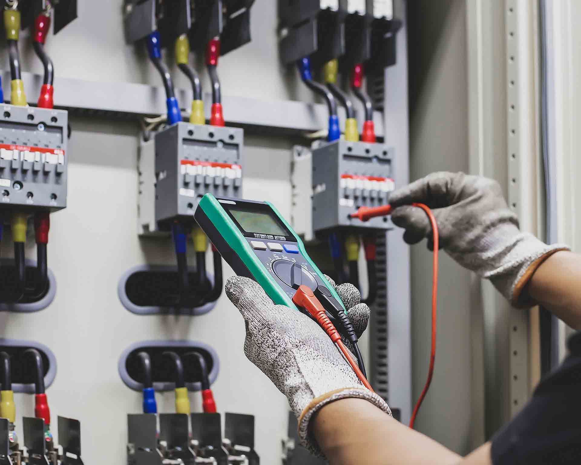A Person is Holding a Multimeter in Front of an Electrical Panel — Eco Sparks Solar & Electrical Contractors in Palmerston, NT