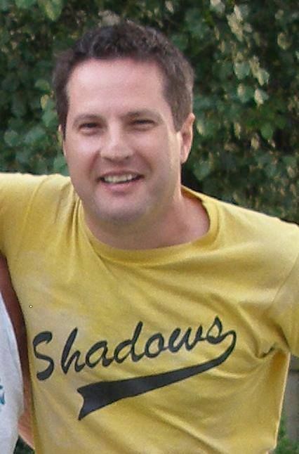 A man wearing a yellow shirt with the word shadows on it