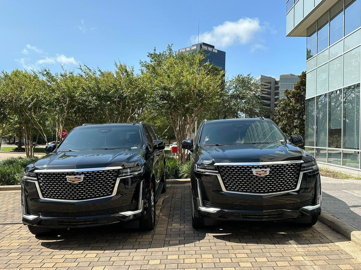 Two black cadillacs are parked next to each other in a parking lot.