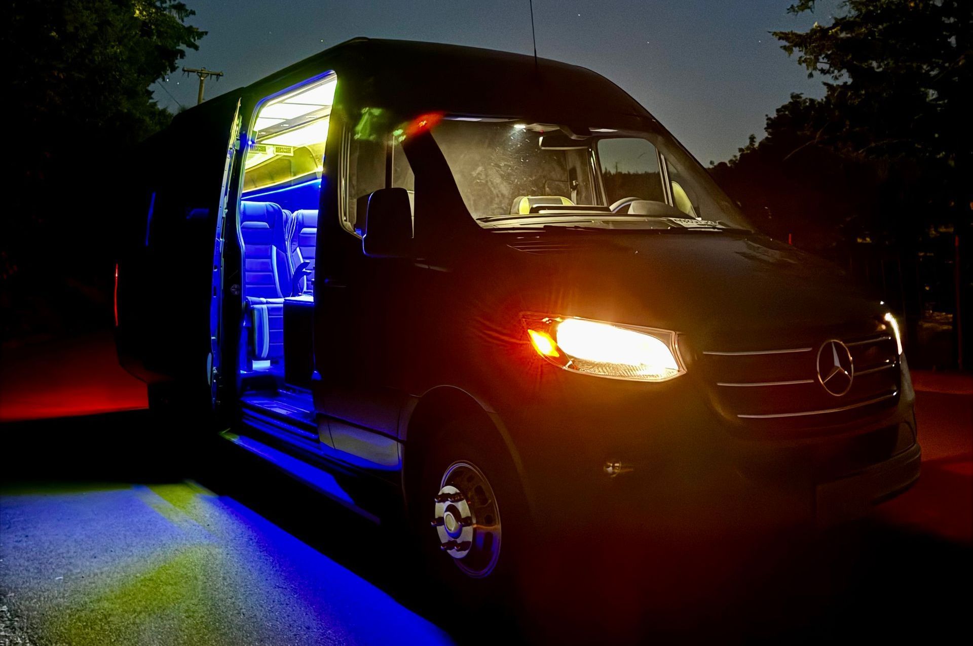 A mercedes van is lit up at night with blue and red lights.