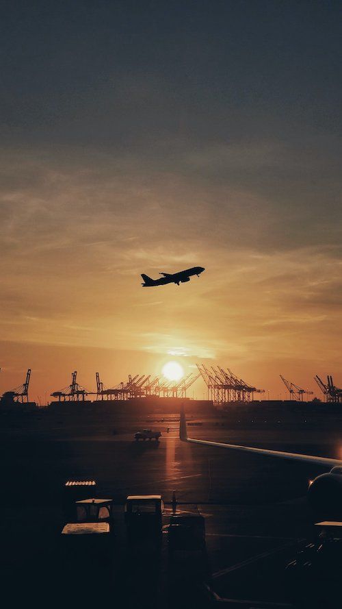 A plane is flying over an airport at sunset.