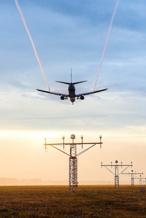 A plane is flying over an airport runway at sunset.