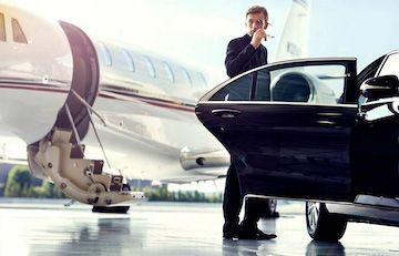 A man is standing next to a car and a private jet.