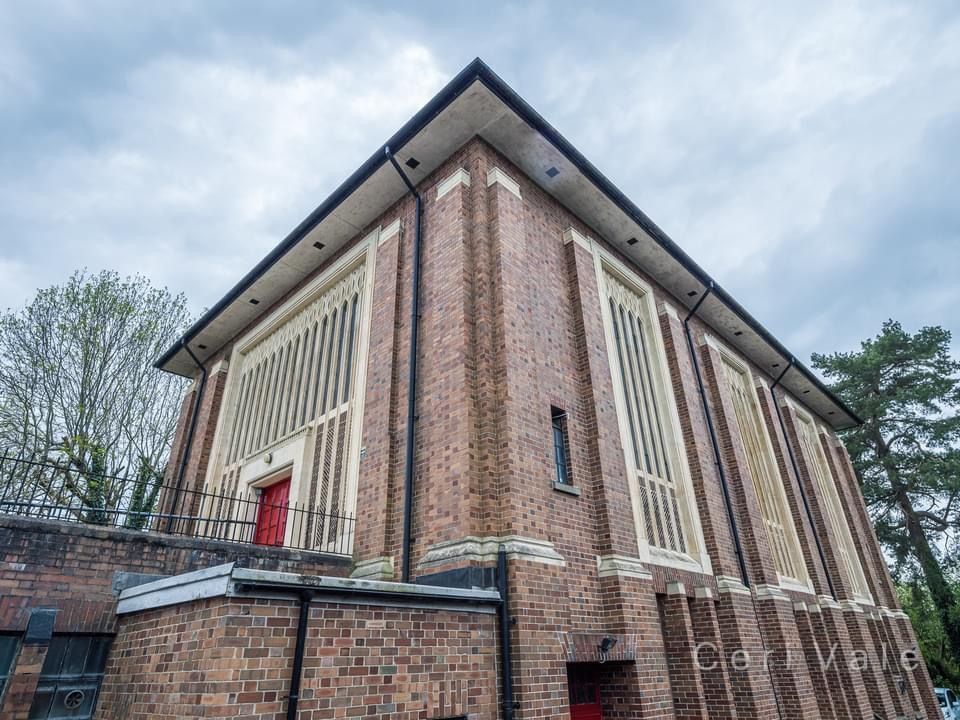 A brick building with a red door is surrounded by trees on a cloudy day.