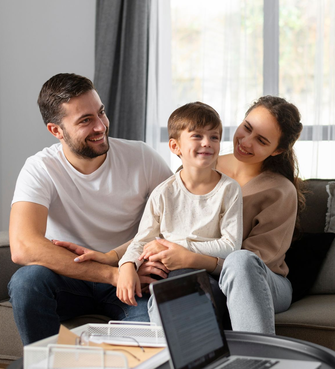 Family sitting on a couch, smiling together in a bright living room.