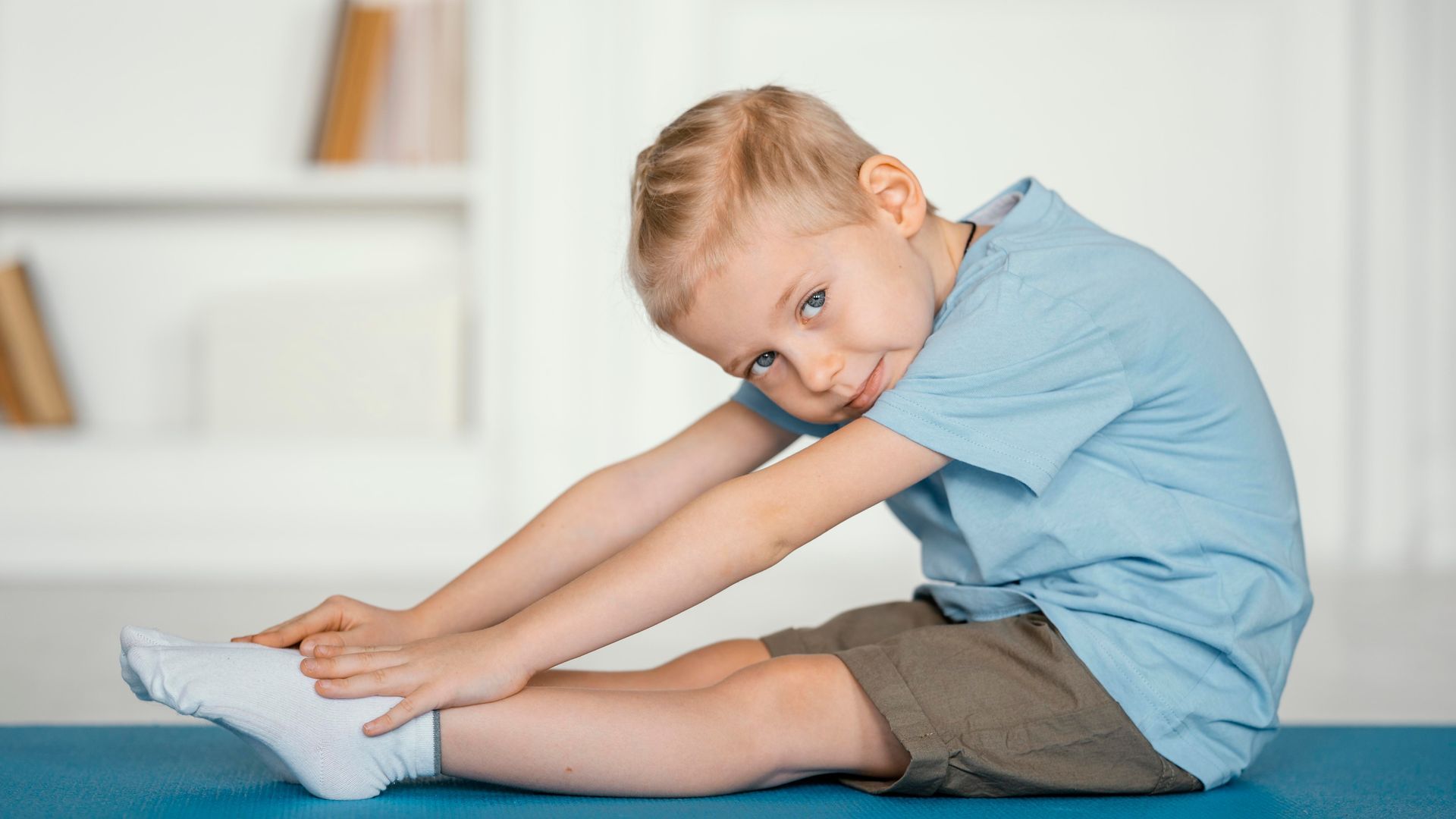 Child stretching toward toes on a blue mat in a bright room