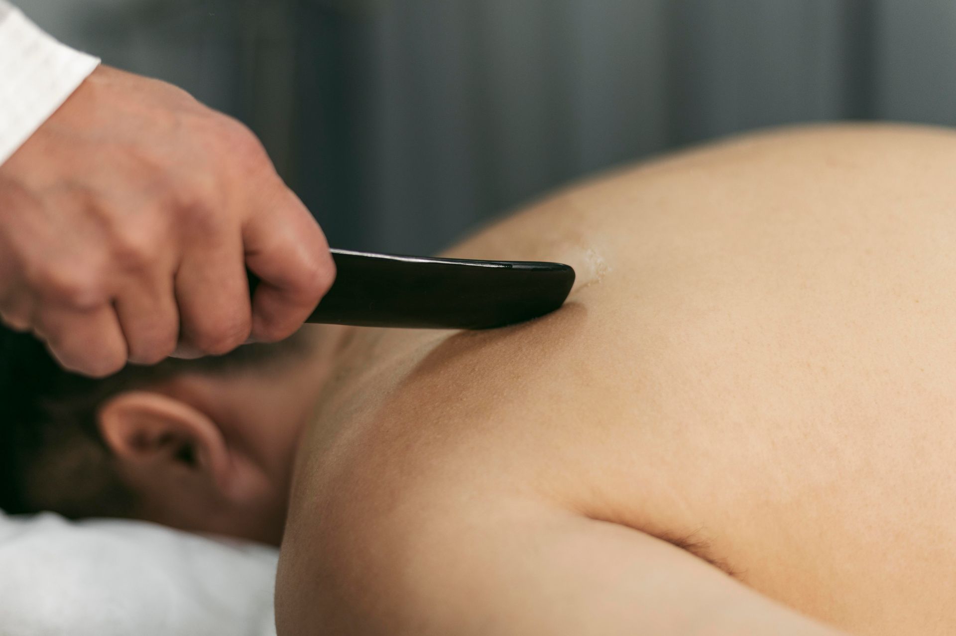 Hand holding a black gua sha tool on a person’s bare back during massage