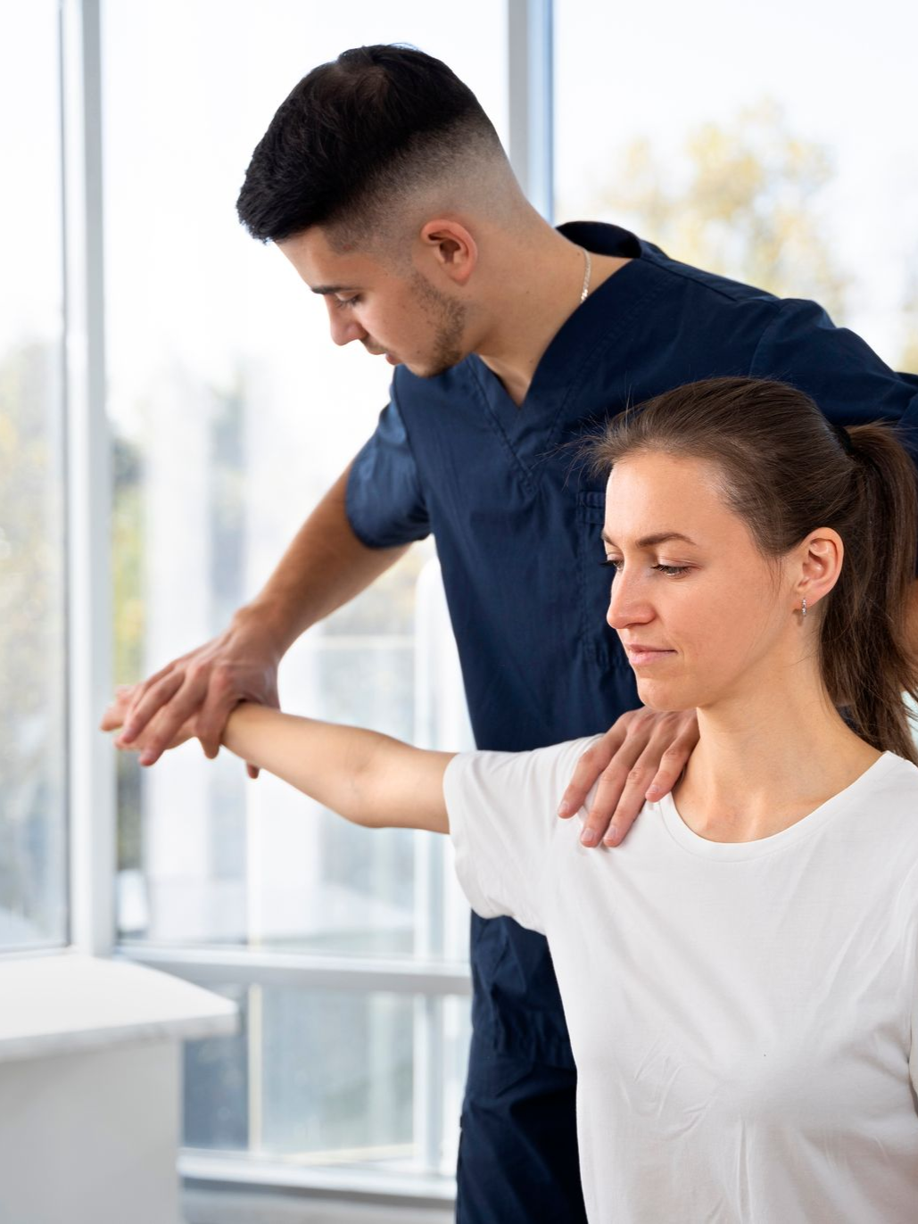 Trainer assisting woman with arm stretch in a bright studio, both focused on the exercise.