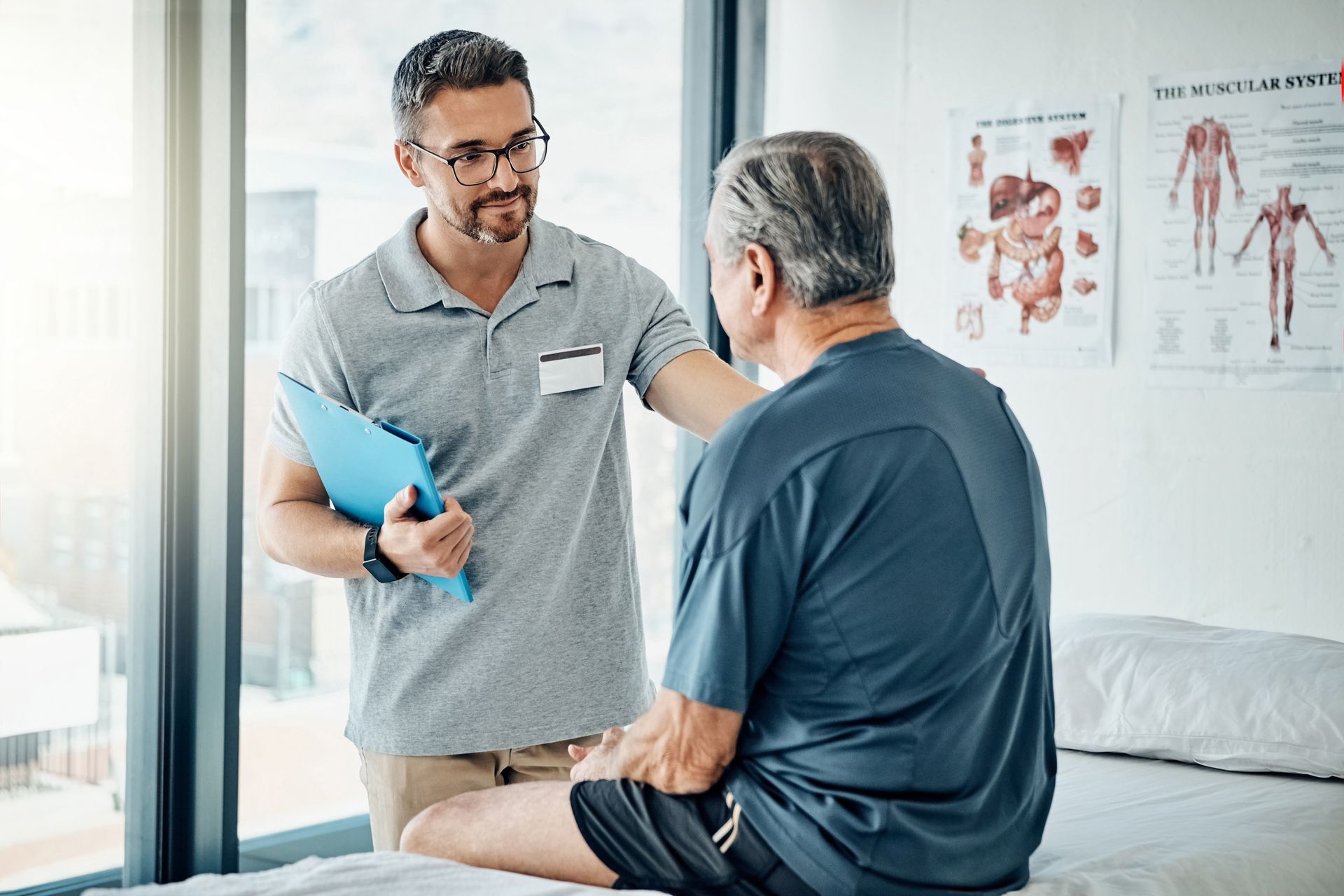 Doctor holding a blue folder talks to a seated patient in a bright clinic office