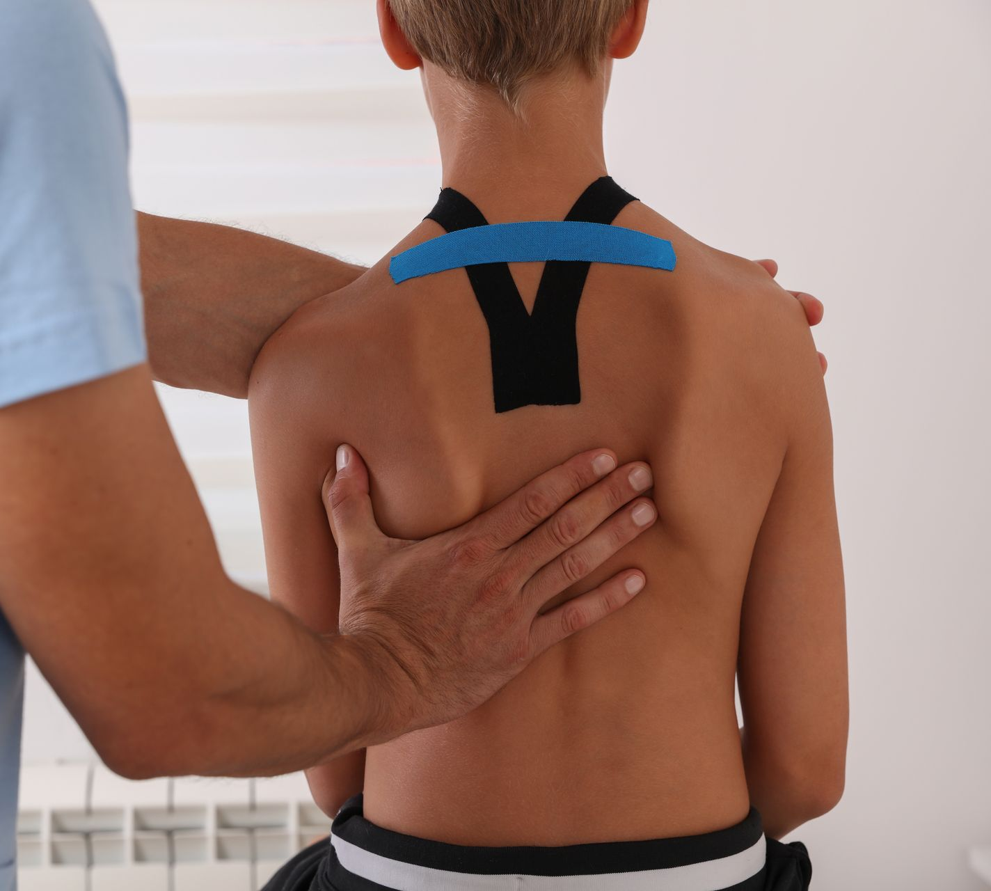 Physical therapist applying kinesiology tape to a child's upper back and shoulders